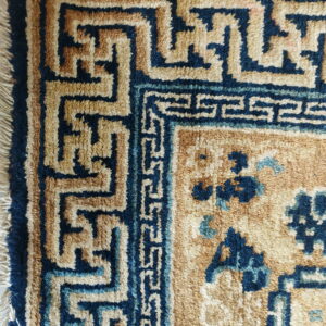 Medium-pile rug detail featuring a navy blue and tan geometric key border and floral field.