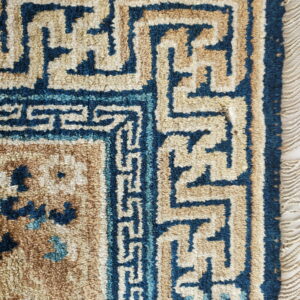 Detail of a high-pile rug with blue and tan geometric fretwork border and visible fringe.