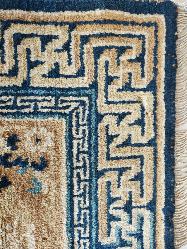 Detail of a high-pile rug with blue and tan geometric fretwork border and visible fringe.
