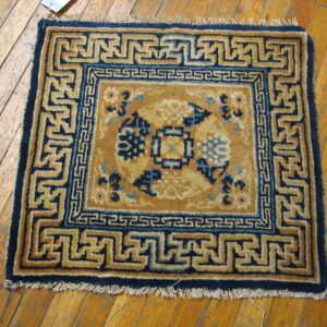 Gold and navy rug featuring geometric meander borders and floral patterns sits on distressed wood planks.
