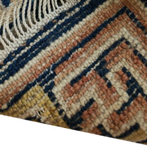 Textured rug corner showing navy, terracotta, cream, and beige geometric patterns with chunky fringe.
