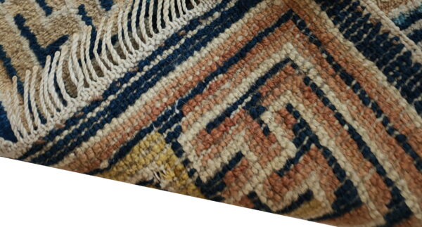 Textured rug corner showing navy, terracotta, cream, and beige geometric patterns with chunky fringe.