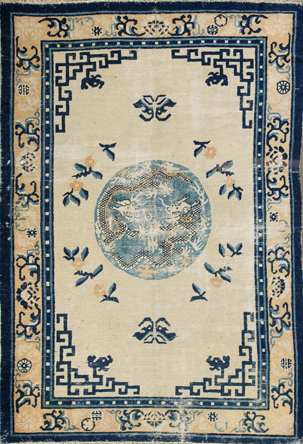 Cream rug with a central blue dragon medallion and repeating navy geometric key pattern border.