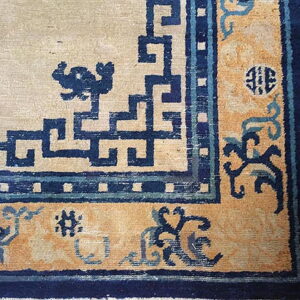 High-contrast rug corner featuring a cream field surrounded by navy blue geometric patterns and a gold pictorial border.