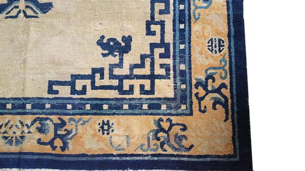 High-contrast rug corner featuring a cream field surrounded by navy blue geometric patterns and a gold pictorial border.