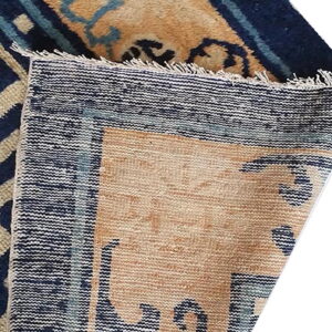 Beige and navy blue patterned rug corner folded over, displaying the woven back and fringe edge.