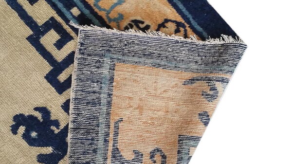 Beige and navy blue patterned rug corner folded over, displaying the woven back and fringe edge.