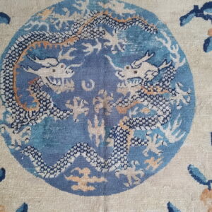 Detailed view of a beige rug with a blue central medallion containing two stylized white and dark blue dragons.