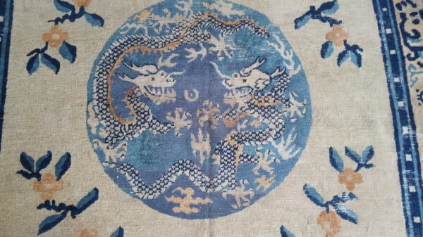 Detailed view of a beige rug with a blue central medallion containing two stylized white and dark blue dragons.