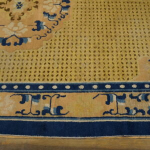 Yellow rug detail showing a spotted field, navy blue borders, and peach floral motifs over wood planks.