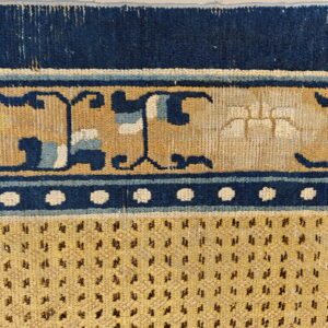 Detailed view of a blue and tan rug with stylized scroll borders and a densely speckled field.