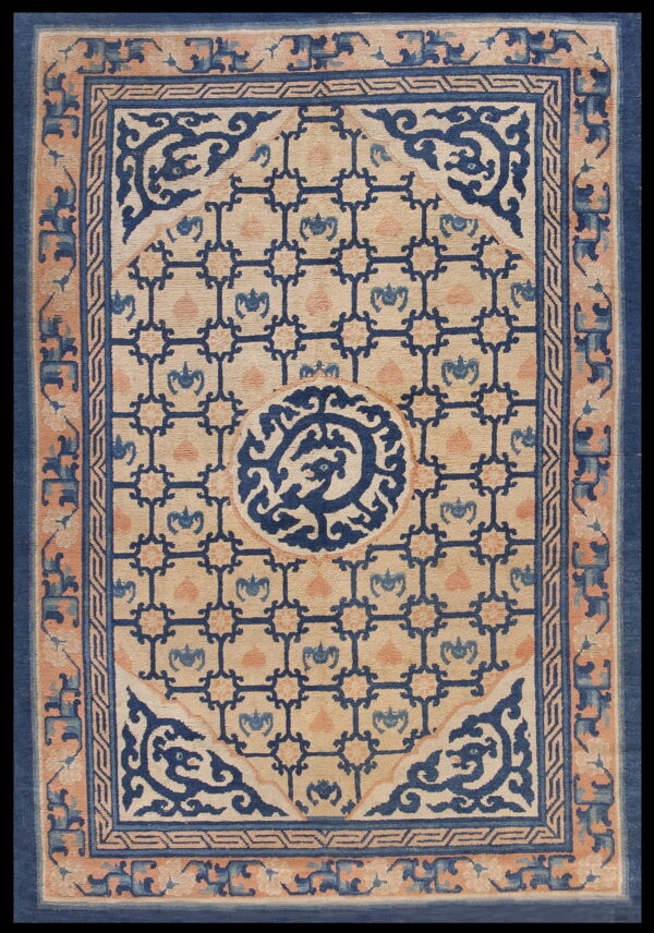 Beige rug with a dark blue geometric lattice and center medallion, bordered by peach and blue scrollwork.