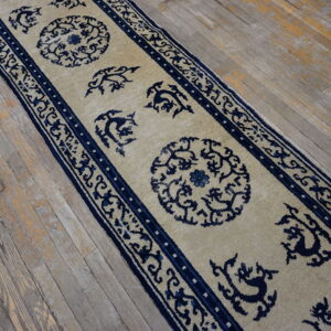 Beige runner rug with ornate dark blue medallions and motifs rests on worn wood flooring.