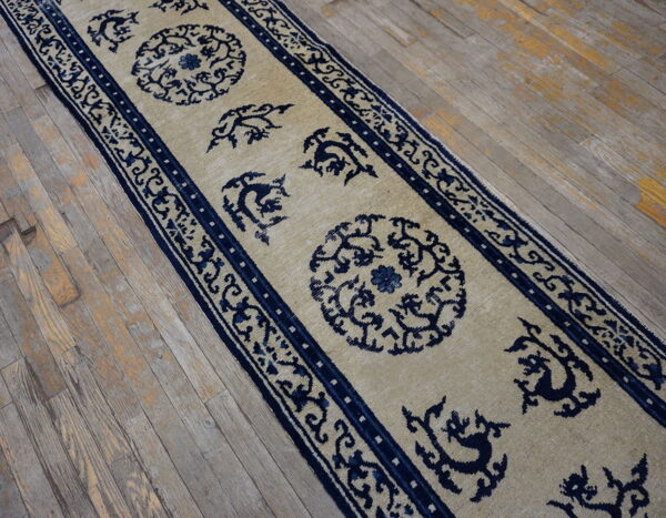 Beige runner rug with ornate dark blue medallions and motifs rests on worn wood flooring.