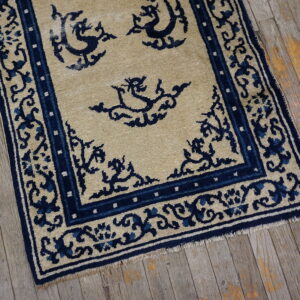 Low-pile tan rug with high-contrast navy blue stylized patterns and border on rustic wood floors.