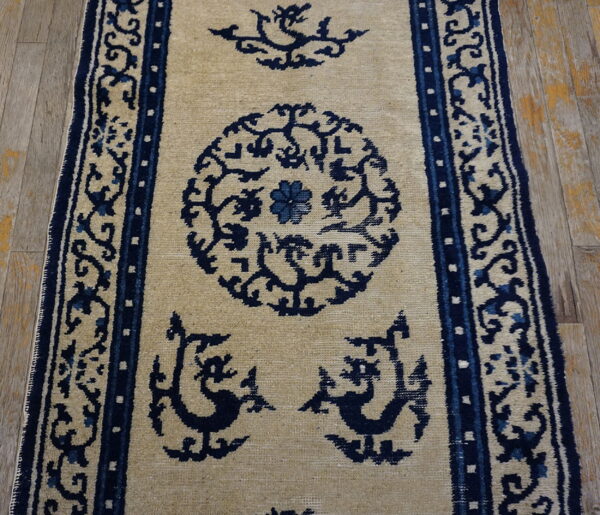 Beige runner rug featuring stylized dark blue medallions, mythological figures, and borders on wood planks.