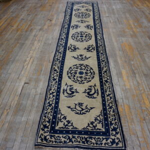Beige and navy blue runner rug with medallions and stylized motifs resting on distressed wood floorboards.