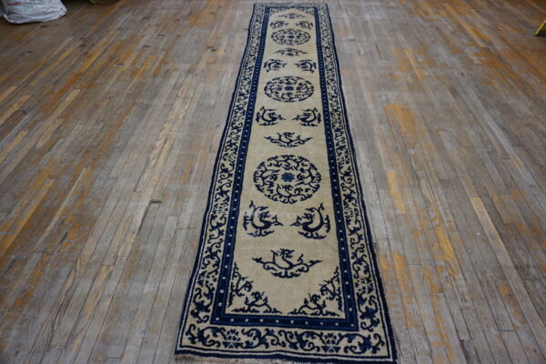 Beige and navy blue runner rug with medallions and stylized motifs resting on distressed wood floorboards.