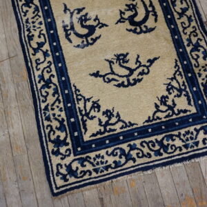 A low pile beige rug with navy stylized patterns and borders sits on distressed gray wood flooring.