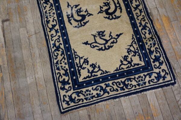 A low pile beige rug with navy stylized patterns and borders sits on distressed gray wood flooring.