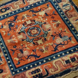 Low pile rug in burnt orange and indigo blue with geometric and floral patterns on wood.