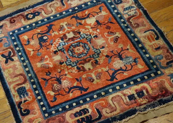 Low pile rug in burnt orange and indigo blue with geometric and floral patterns on wood.