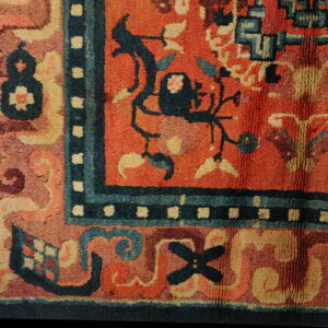 Thick-pile rug detail showing orange, indigo, and cream stylized patterns within multiple borders.
