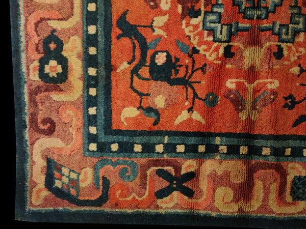 Thick-pile rug detail showing orange, indigo, and cream stylized patterns within multiple borders.
