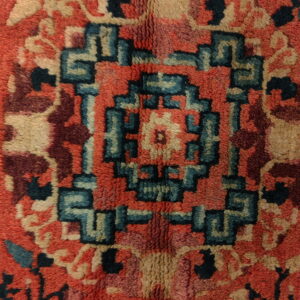 Textured high-pile rug detail showing a central stepped geometric pattern in teal, tan, red, and maroon.