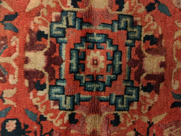 Textured high-pile rug detail showing a central stepped geometric pattern in teal, tan, red, and maroon.