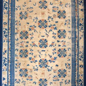 Beige and blue patterned rug featuring floral motifs and a Greek key border on wide plank hardwood flooring.