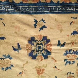 Beige field rug with blue and rust floral patterns and a dark blue Greek key border.