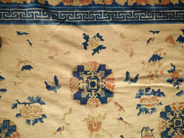 Beige field rug with blue and rust floral patterns and a dark blue greek key border.