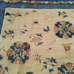 Worn beige rug featuring scattered blue and rust motifs and a prominent dark blue geometric border.