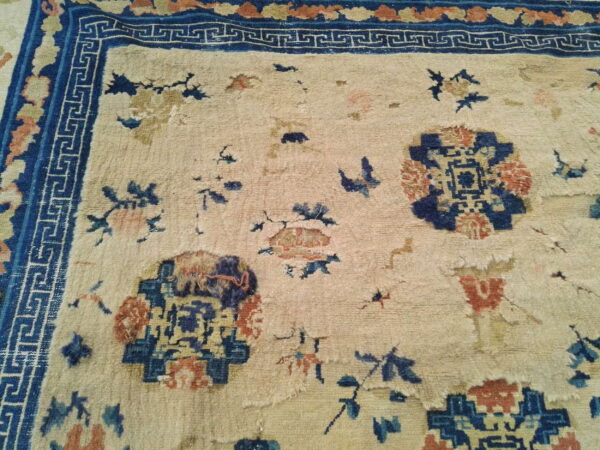 Worn beige rug featuring scattered blue and rust motifs and a prominent dark blue geometric border.