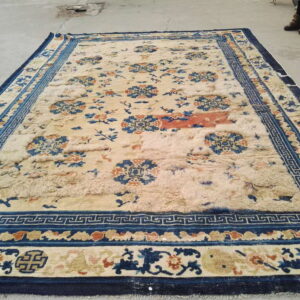 Large cream rug with navy, blue, and orange florals, featuring distressed pile on a concrete floor.