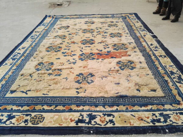 Large cream rug with navy, blue, and orange florals, featuring distressed pile on a concrete floor.