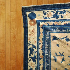 Cream rug with intricate dark blue geometric and floral borders lies across light wood flooring.