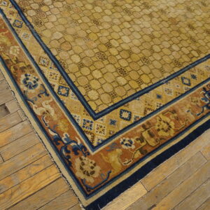 A gold geometric rug with navy and rust floral borders lies on distressed wooden floorboards.