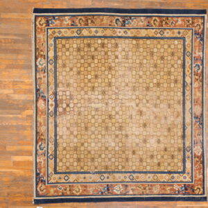 Square beige rug featuring an interlocking geometric field and wide rust and navy floral borders over wood floors.