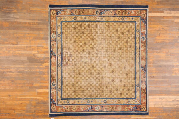 Square beige rug featuring an interlocking geometric field and wide rust and navy floral borders over wood floors.