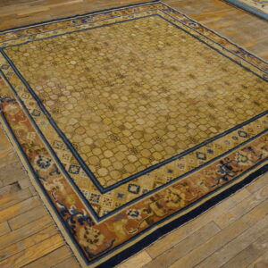 Gold rug with honeycomb pattern and navy, terracotta, and yellow borders on distressed wood floor.