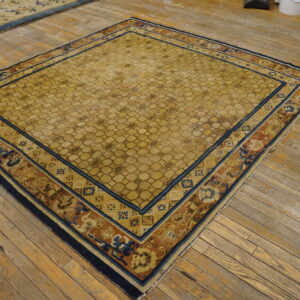 Gold rug featuring a honeycomb pattern and elaborate borders in navy, rust, and blue on wood flooring.