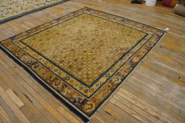 Gold rug featuring a honeycomb pattern and elaborate borders in navy, rust, and blue on wood flooring.