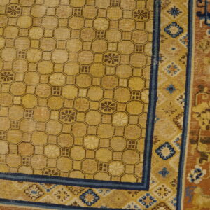 Golden yellow rug featuring a dark geometric lattice pattern and complex blue and rust floral borders on wood flooring.