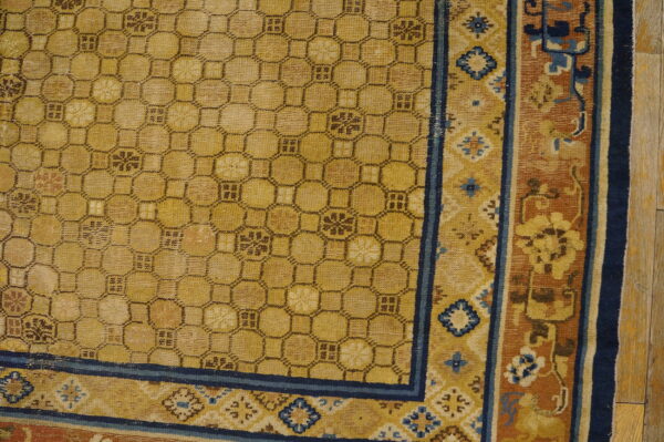 Golden yellow rug featuring a dark geometric lattice pattern and complex blue and rust floral borders on wood flooring.