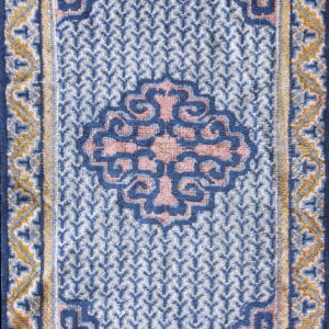 A rectangular blue, white, pink, and gold patterned rug with a visible thick pile texture and detailed borders.