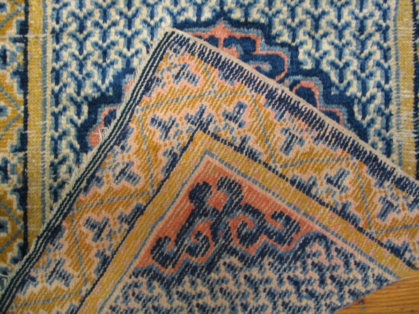 A rug is folded over, showing its woven foundation and geometric patterns in blue, gold, and coral.