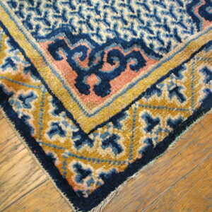 Geometric and stylized rug corner in blue, gold, and pink rests on textured wood planks.