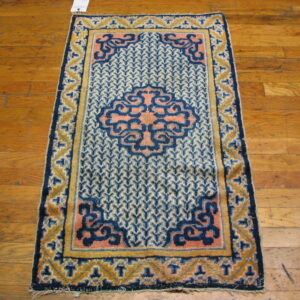 Low-pile rug in navy blue, pale blue, pink, and gold with ornate borders on distressed hardwood.